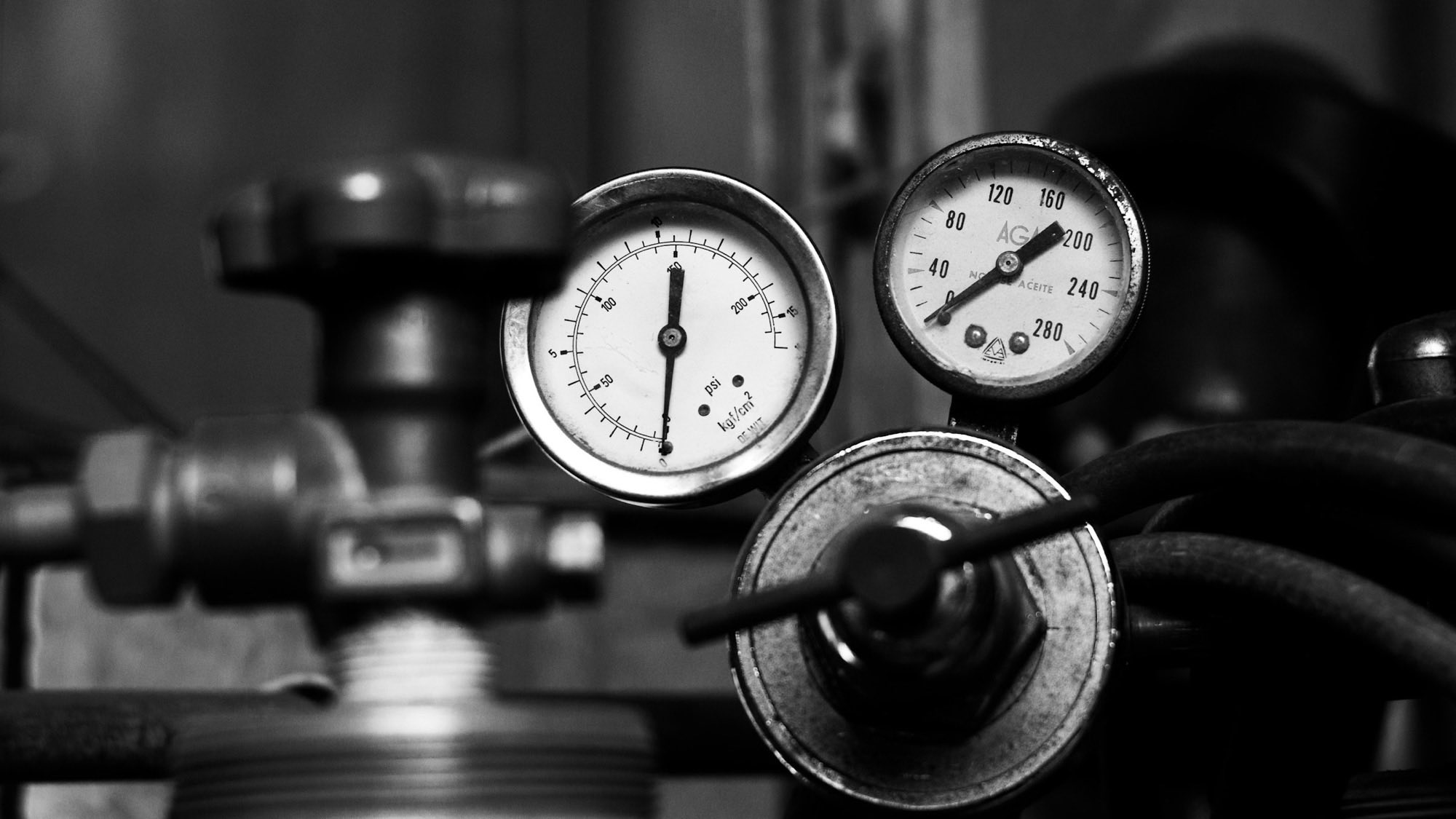 Two analogue pressure gauges on industrial valves in black and white, each needle resting at a different reading